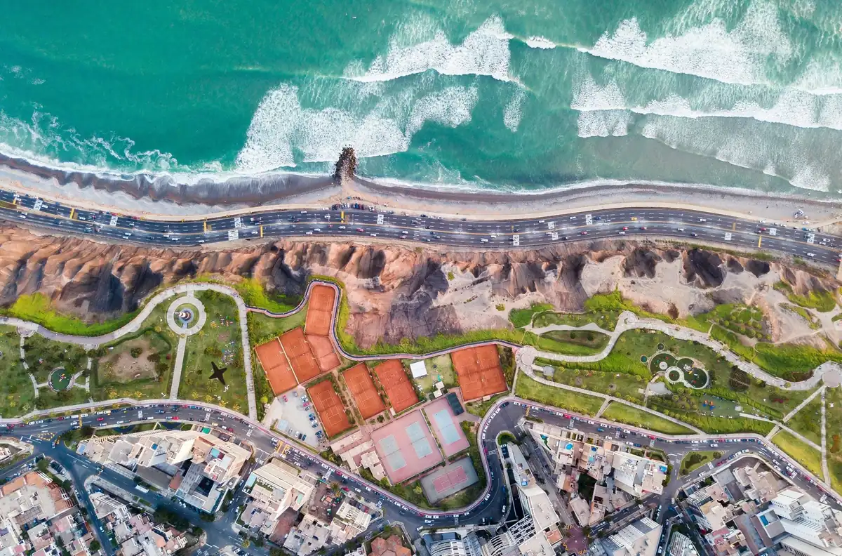Vista aérea del litoral de Miraflores, en Lima, con olas del océano, acantilado, parque con canchas de tenis y calles